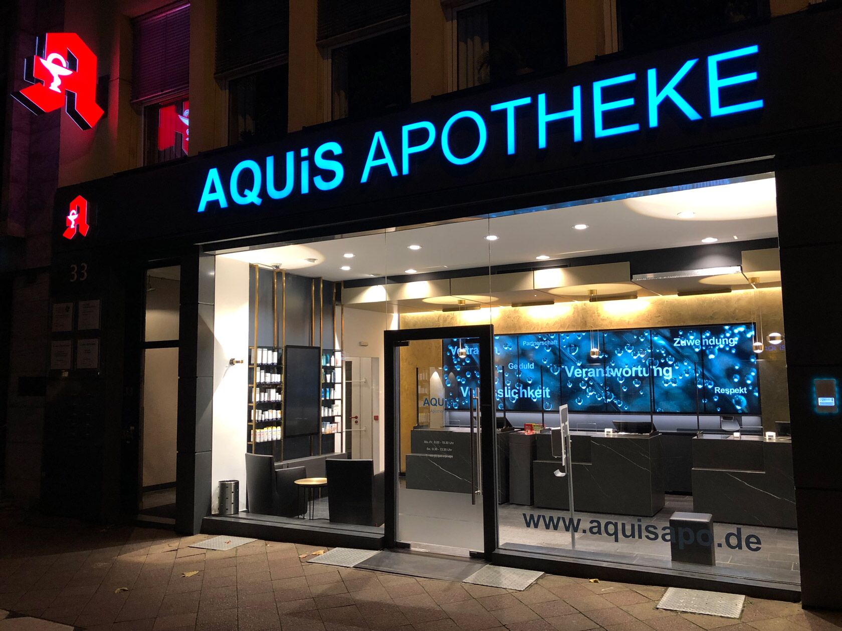 Eine moderne Apotheke mit beleuchtetem Schild zeigt eine einladende Glasfassade bei Nacht.