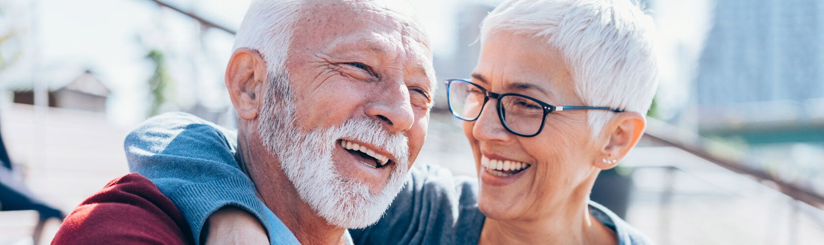 Zwei Senioren lachen herzlich im Sonnenschein und zeigen den Schwerpunkt auf Lebensfreude im Alter.