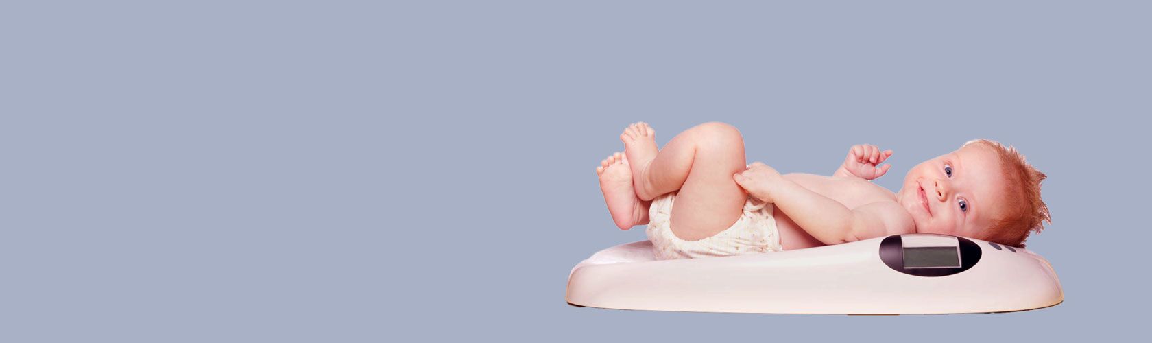 Ein lächelndes Baby liegt entspannt auf einer Babywaage, die auf einem hellblauen Hintergrund steht.