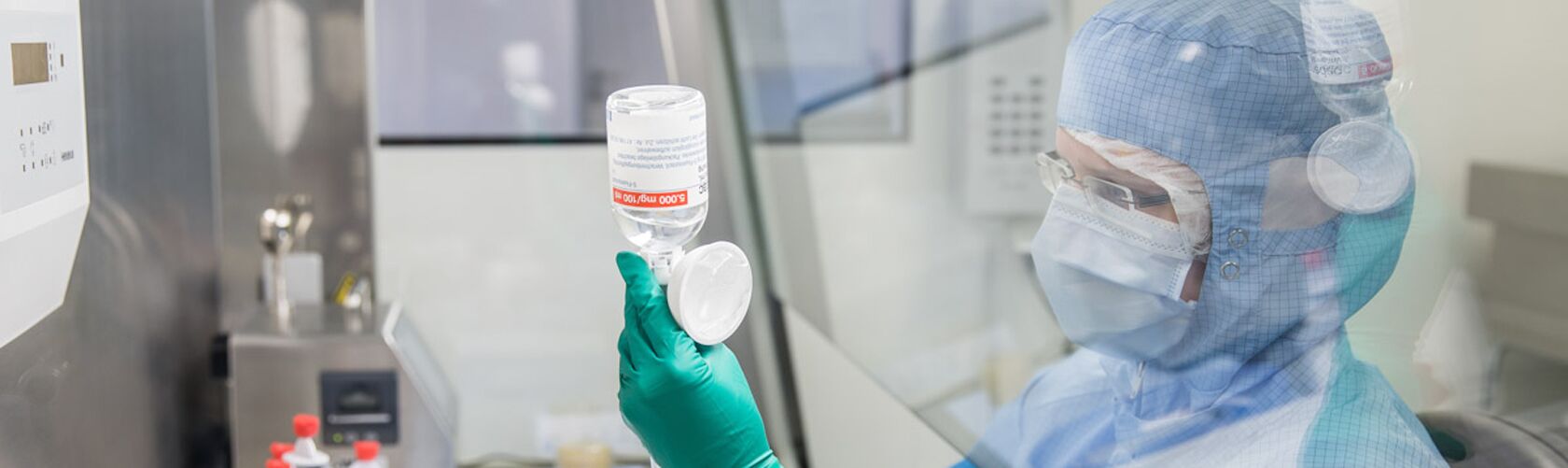 Eine medizinische Fachkraft in Schutzkleidung untersucht eine Flasche in einem Labor mit Schwerpunkt auf Onkologie.